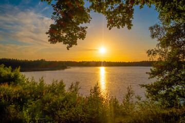 Panorama of a gorgeous sunset at a forest lake, with gold and blue color in the sky and trees reflected in the water. High quality photo