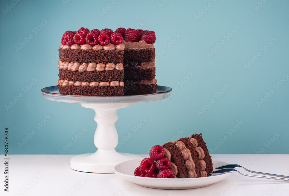 Sticker Chocolate birthday cake with raspberries and butter cream on  white table and blue background. Piece of cake on a plate. Copy space.