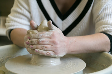 Potter girl works on a Potter's wheel, making a ceramic pot out of clay in a pottery workshop
