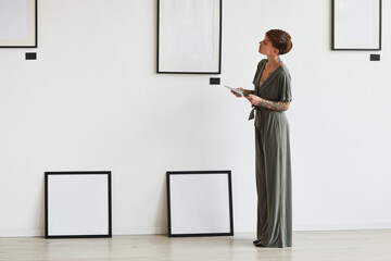 Graphic full length portrait of elegant female art gallery manager looking at frame setting while...