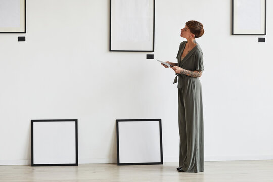 Graphic full length portrait of elegant female art gallery manager looking at frame setting while planning exhibition or event, copy space