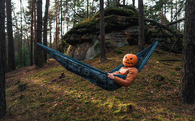 Halloween Scarecrow with a carved pumpkin in relax in Hammocks on trees in the forest it seems they...