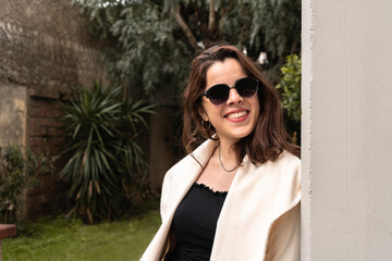 Outdoor girl with dark sunglasses leaning on a column and smiling