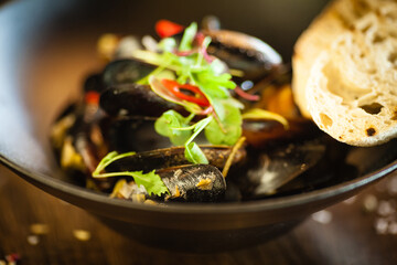 Blue mussels in white wine sauce in black bowl. Delicious healthy seafood closeup served on a table for lunch in modern cuisine gourmet restaurant