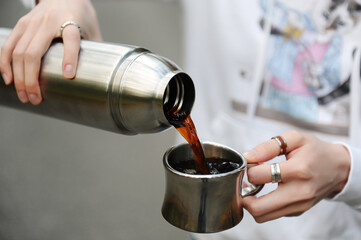 Coffee in travel. Girl pouring hot black coffee from thermos outdoor. Close up