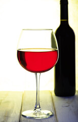 A thin-stemmed glass of red wine.A bottle of wine in the background.