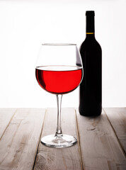 A thin-stemmed glass of red wine.A bottle of wine in the background.