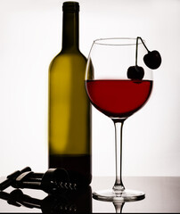 A thin-stemmed glass with red wine and a cherry on the edge.