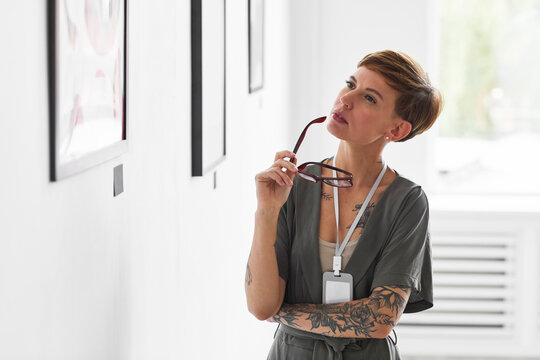 Waist up portrait of elegant creative woman looking at paintings while visiting modern art gallery exhibition, copy space
