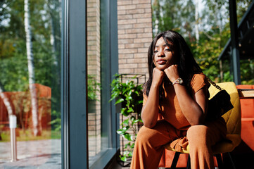 Portrait of beauty young black woman, wear orange outfit, pose at restaurant.