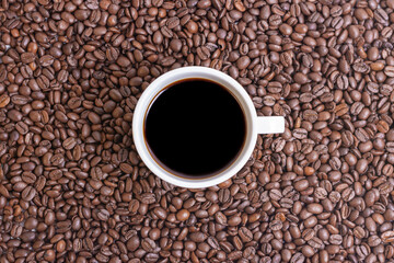 TOP VIEW OF A COFFEE BEANS BACKGROUND AND A FULL CUP OF COFFEE IN THE MIDDLE
