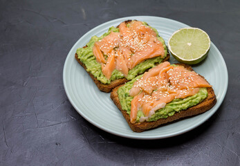 Toasted bread with avocado, red fish on dark background. Breakfast