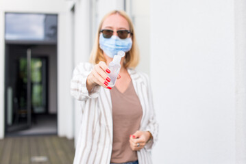 A young woman in an anti-covid mask stands on a terrace of her house, holding a disinfectant gel in her hands. Woman in terrace with sanitizer gel. Woman in quarantine on terrace. Pandemic theme