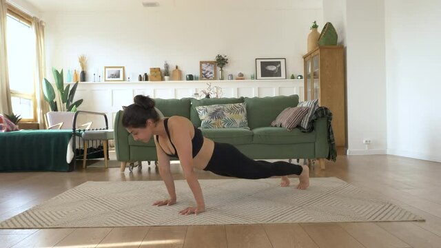 Girl is stretching on carpet in living room. Sporty woman is doing yoga poses in dynamic, down face dog and upward facing dog poses. Sport and home fitness. Training, workout and wellness concept.