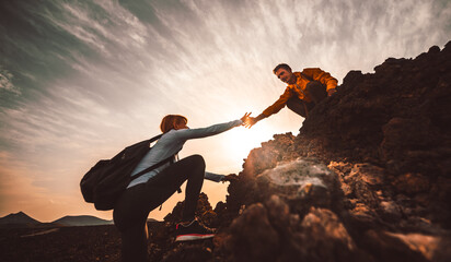 Couple of hikers helping each other climbing a mountain at sunset. People giving a helping hand and...