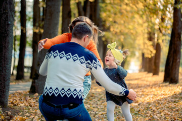 Smiling young family running into leaves on autumns day. active games