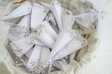 Eleganti porta riso bianchi con bordo in pizzo appoggiati su una tovaglietta in un cestino in attesa del lancio agli sposi