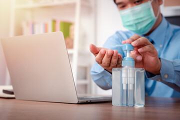 Businessman wearing a mask and use hand sanitizer on his desk for prevention or antibacterial hygiene and Coronavirus disease at the office.