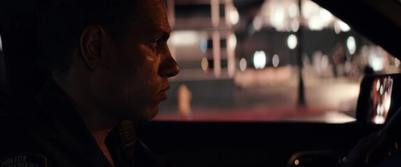 CU Portrait of African-American Black officer driving in a vehicle through city streets at night. Shot on RED Dragon with 2x Anamorphic lens