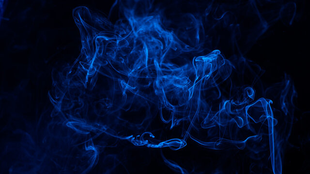 Conceptual image of blue color smoke isolated on dark black background.