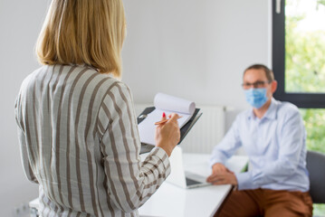 Obraz premium The woman is giving a presentation and the man wearing the face mask. Two business colleagues wearing protective face mask on a meeting during coronavirus. Work in a corporation during a pandemic. 