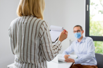 Fototapeta premium The woman is giving a presentation and the man wearing the face mask. Two business colleagues wearing protective face mask on a meeting during coronavirus. Work in a corporation during a pandemic. 