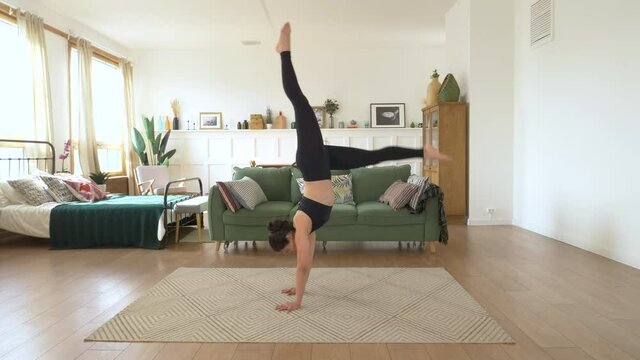 A young Indian gymnast Ballerina trains at home, Doing a Handstand exercise, a Bright cozy Room, Dressed in a Black Top and Leggings. Sports Concept Healthy Life