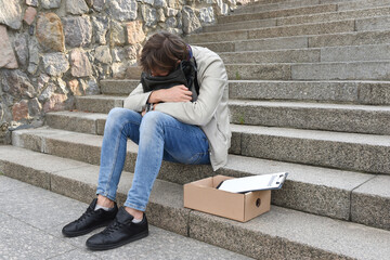 Unemployment and layoffs concept. An employee of the company, having lost his job, sitting on the stairs in the street in a severe depression. The economic crisis of unemployment.