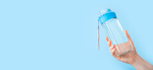 Drinking water bottle for sports in female hand on blue backgraund. Reusable bottle. Healthy lifestyle and fitness concept. Long web banner with copy space