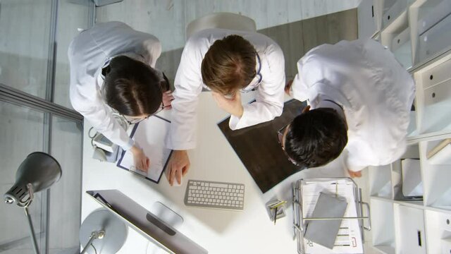 Top view shot of group of physicians in white coats looking at computer screen and talking, then discussing x-ray of patient