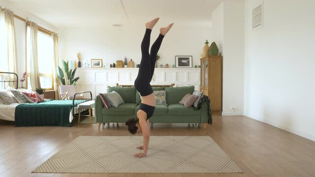 A young Indian Female Ballerina trains at home, Doing a Handstand exercise, a Bright cozy Room, Dressed in a Black Top and Leggings. Sports Concept Healthy Life