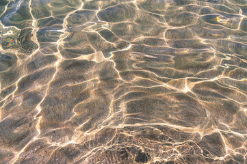 Clear sea water with sun glare and a blurred sandy bottom. Transparent shiny water surface in motion blur