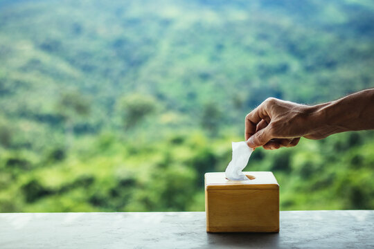 Asian man's hand pull the tissue paper from tissue boxes on wooden table with blur natural mountain view background.