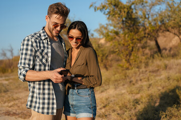 Joyful couple hugging and using cellphone while strolling on nature