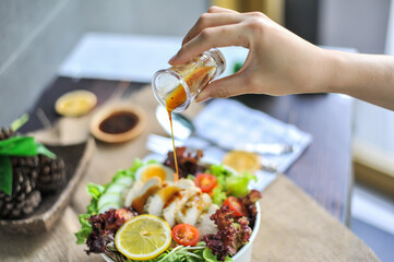 A hand pouring salad dressing into a garden salad