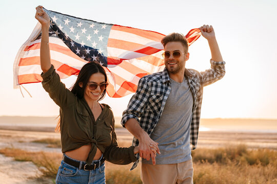 Happy couple holding hands together while strolling with american flag