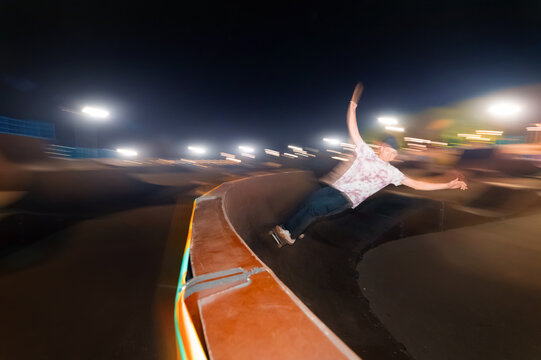 Motion in blur young skater is rolling down the ramp at night in a skate park. Flash technique with wiring movement - Powered by Adobe