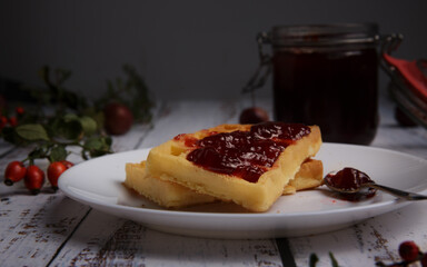 soft waffles smeared with strawberry jam and a glass jar with jam. selective focus 