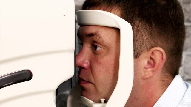Close-up portrait of man during test on refractometer machine, side view. Eye exam for man at optical store.
