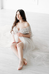 beautiful young pregnant woman in long white dress and sitting on the floor