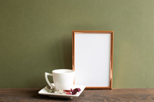Empty photo frame with coffee cup and dry flowers on wooden table with khaki background