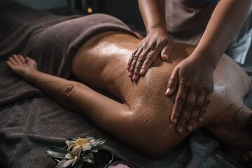 Hands of an Asian masseuse who massages the back of a young man with oil, lying on a massage table, blurred background, wellness center.