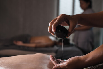 Closeup of masseur hands pouring aroma oil on woman back. Masseuse prepare to do oriental spa...
