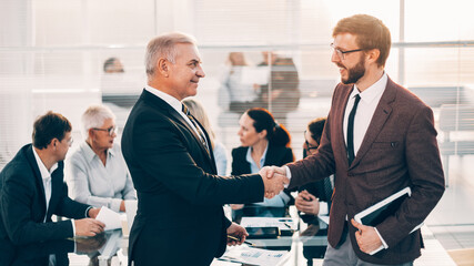 boss shaking hands with an employee near the desktop