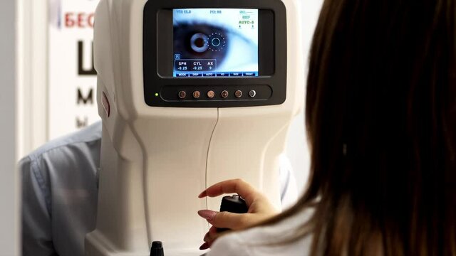 Optician doctor working with the refractometer machine. Eye exam for man at optical store.