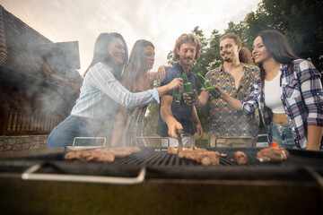 Fototapeta premium Barbecue smoke rising from the ember as it gets greeted with beer and young people