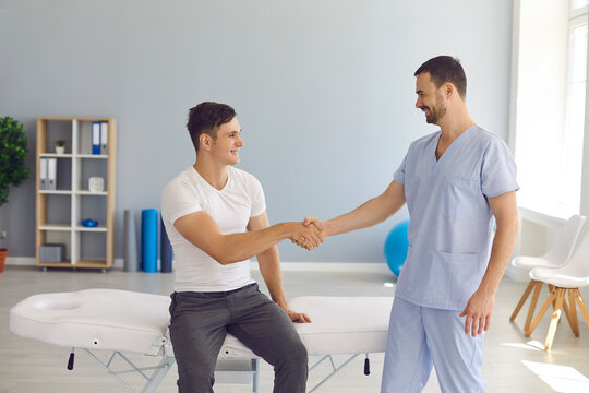 Friendly doctor shaking hands with young patient in massage room of modern hospital