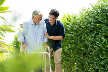 Elderly Asian father and Adult son walking in backyard. Positive Asian man caregiver helping patient