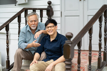 Fototapeta na wymiar Senior Asian Father and Adult Son Relaxing and talking at home outdoors. senior mature father and smiling young adult. Happy family time together.