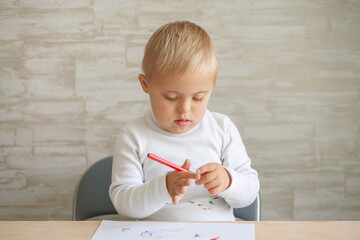 A boy with Down syndrome sits at a large table and draws with felt-tip pens, the child is engaged...